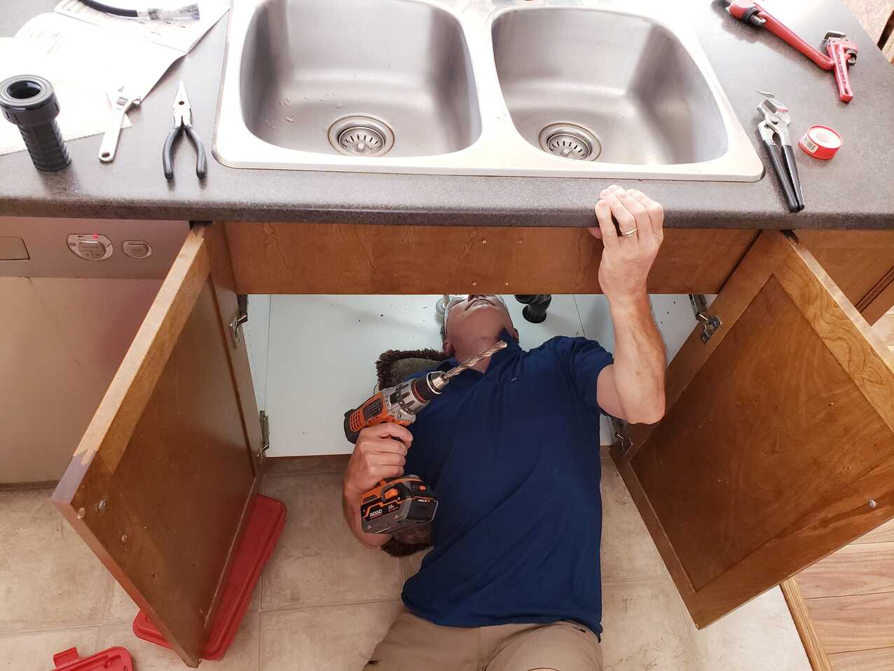 A worker doing repairs on leaking pipe under sink