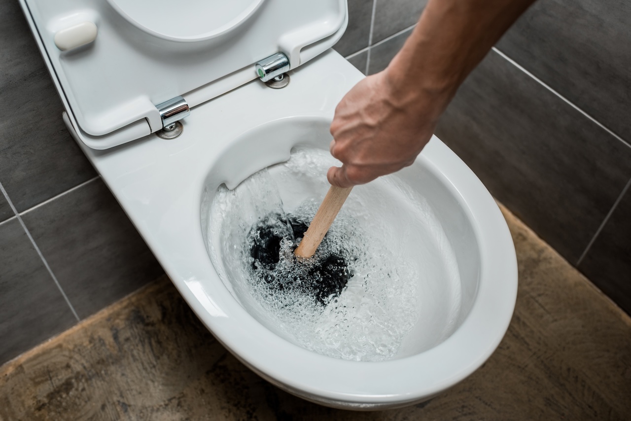 toilet overflowing being cleared with a plunger to stop water from rising